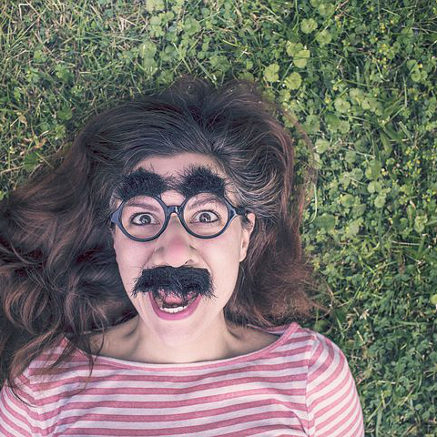 Girl with fake mouatache lying in grass