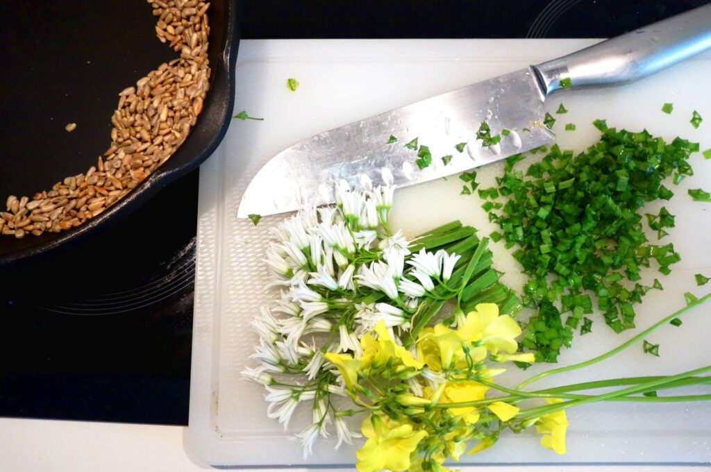 a cutting board with half-chopped wild garlic and oxalis flowers